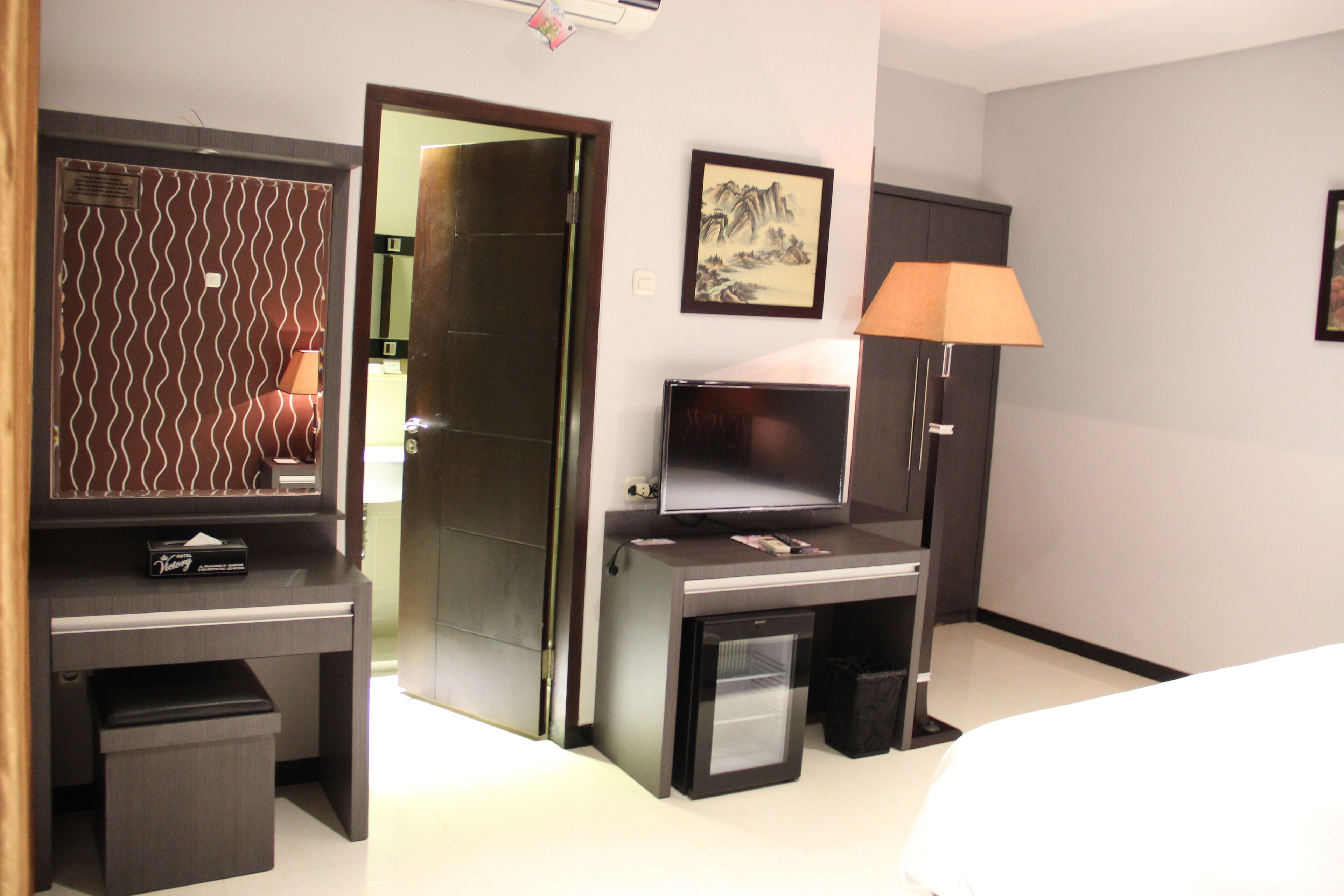 Una habitación de hotel con escritorio, televisión, lámpara, cesto de basura y cama.