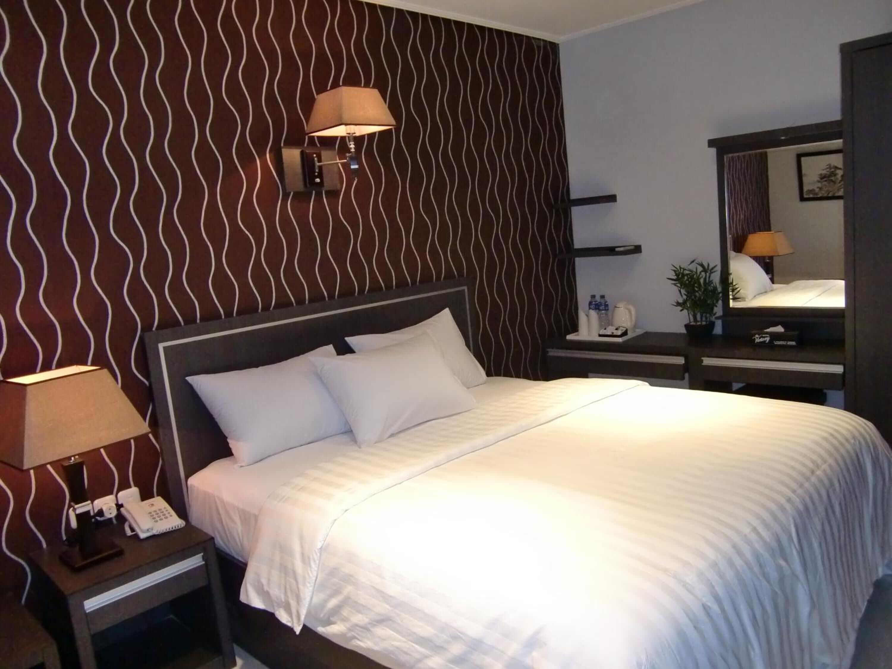 Una habitación de hotel con una cama, una mesita de noche con lámpara, un teléfono y un espejo.