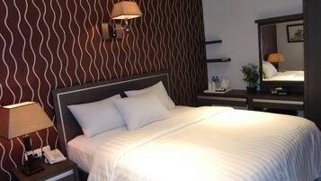 Una habitación de hotel con una cama, una mesita de noche con lámpara, un teléfono y un espejo.
