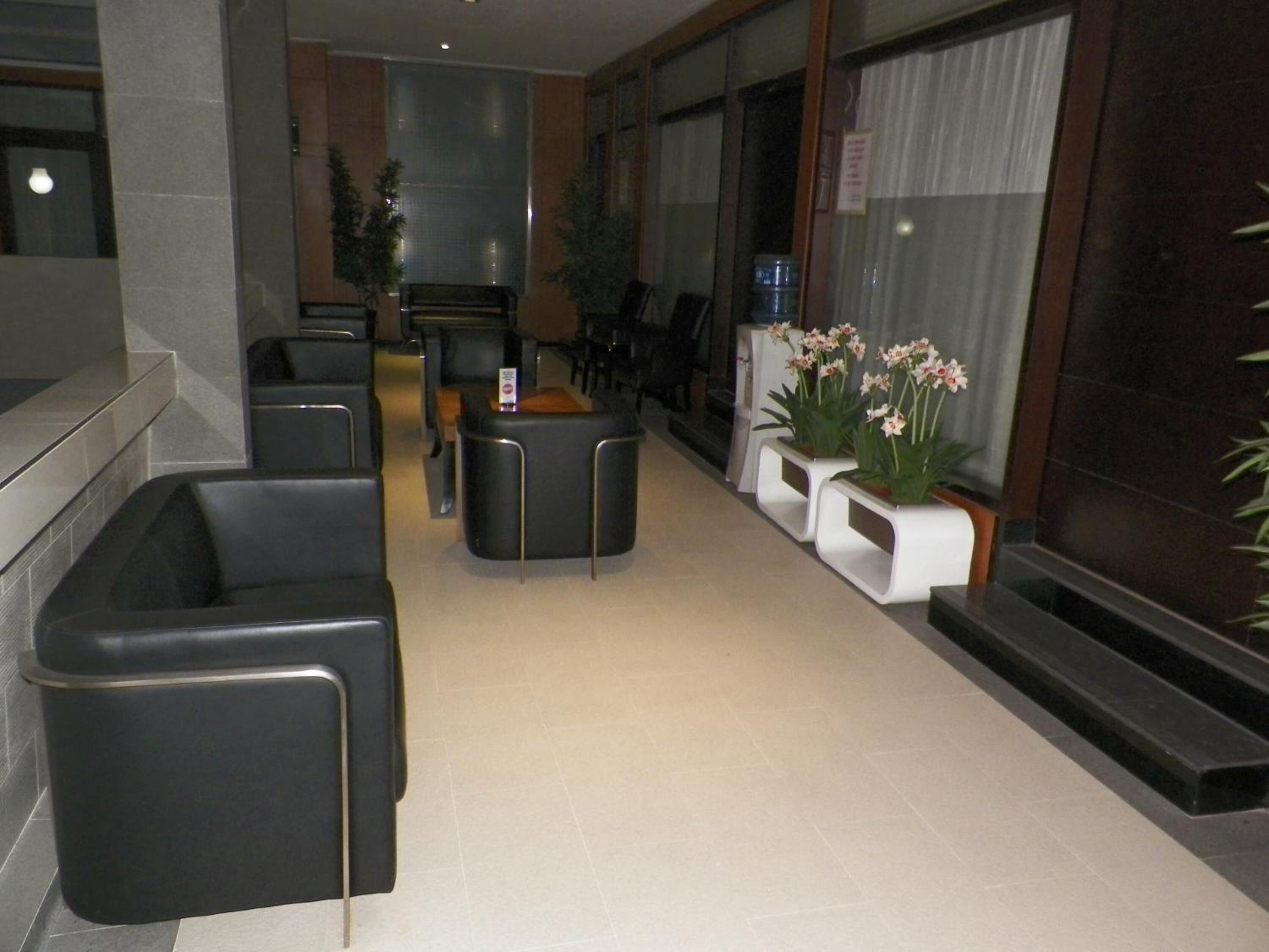 A modern lobby with black leather seating, a reception desk, and potted plants.