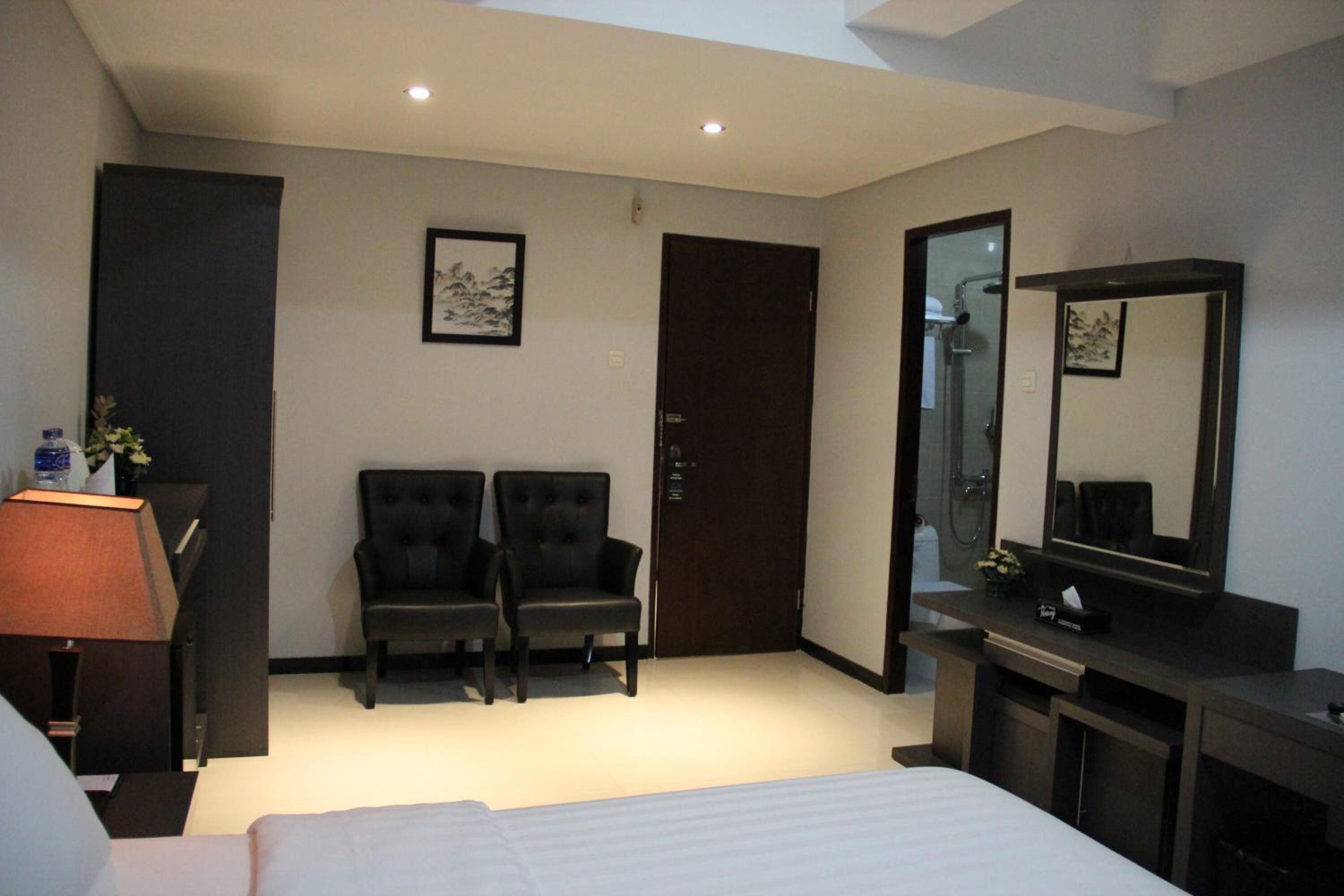 A hotel room with a bed, two armchairs, a desk with a mirror, a lamp, and a door.