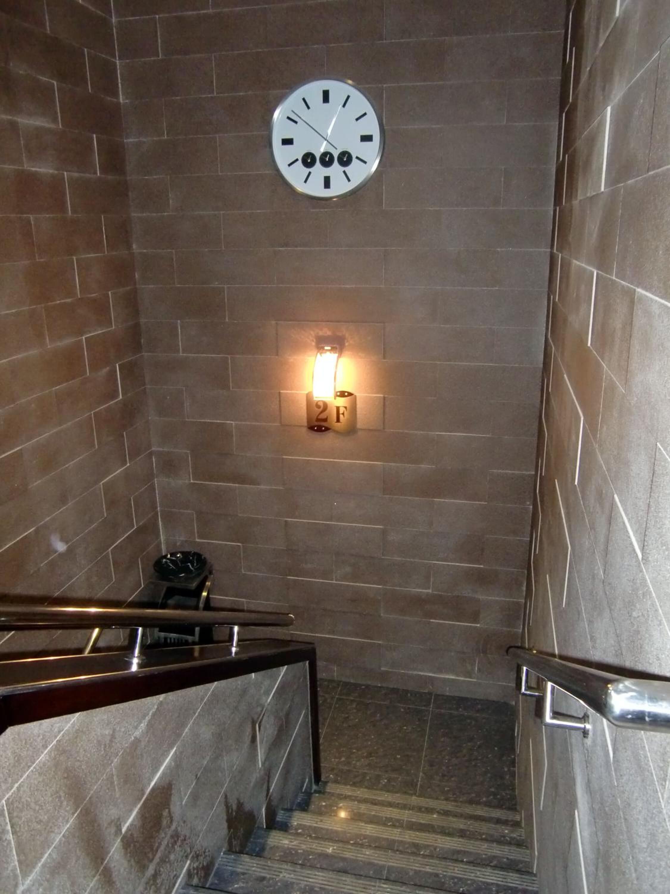 A stairwell with a wall clock, a light fixture, and a fire alarm.