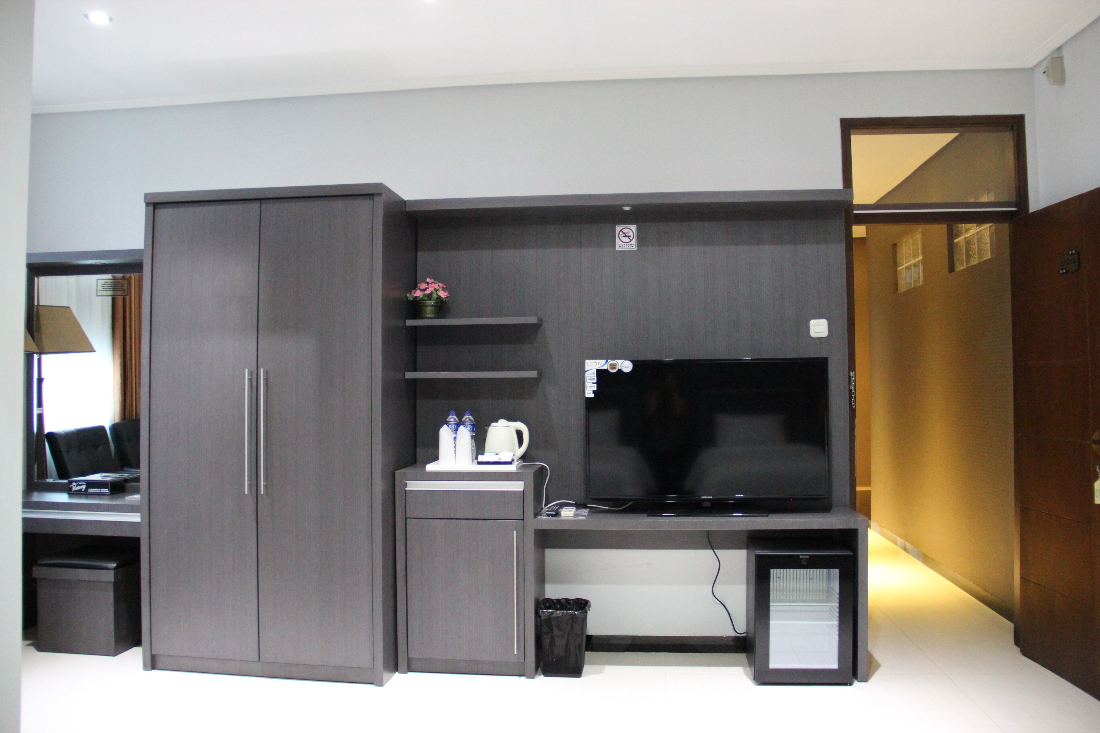 A modern room with a large grey wardrobe, a flat-screen TV, a small shelf with a potted plant, and a desk with a computer.