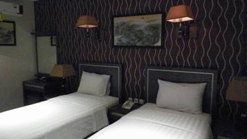 Een hotelkamer met twee eenpersoonsbedden, een nachtkastje met een lamp, een schilderij aan de muur en behang met een patroon.