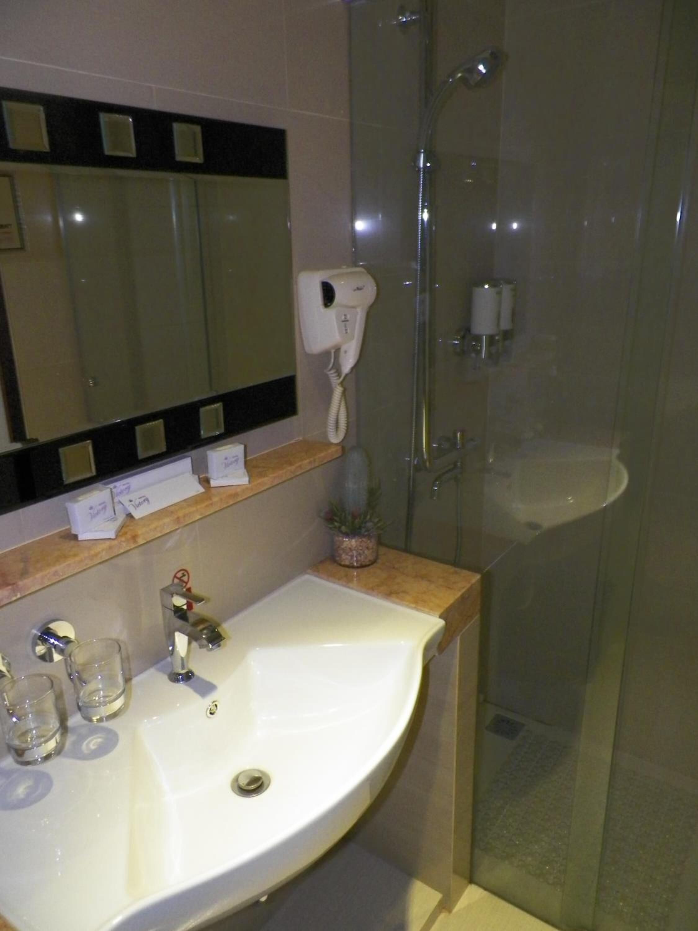 Un baño con lavamanos blanco, espejo, secador de pelo y cabina de ducha de vidrio.