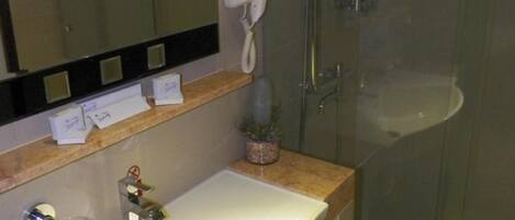 A bathroom with a white sink, a mirror, a hairdryer, and a glass shower enclosure.