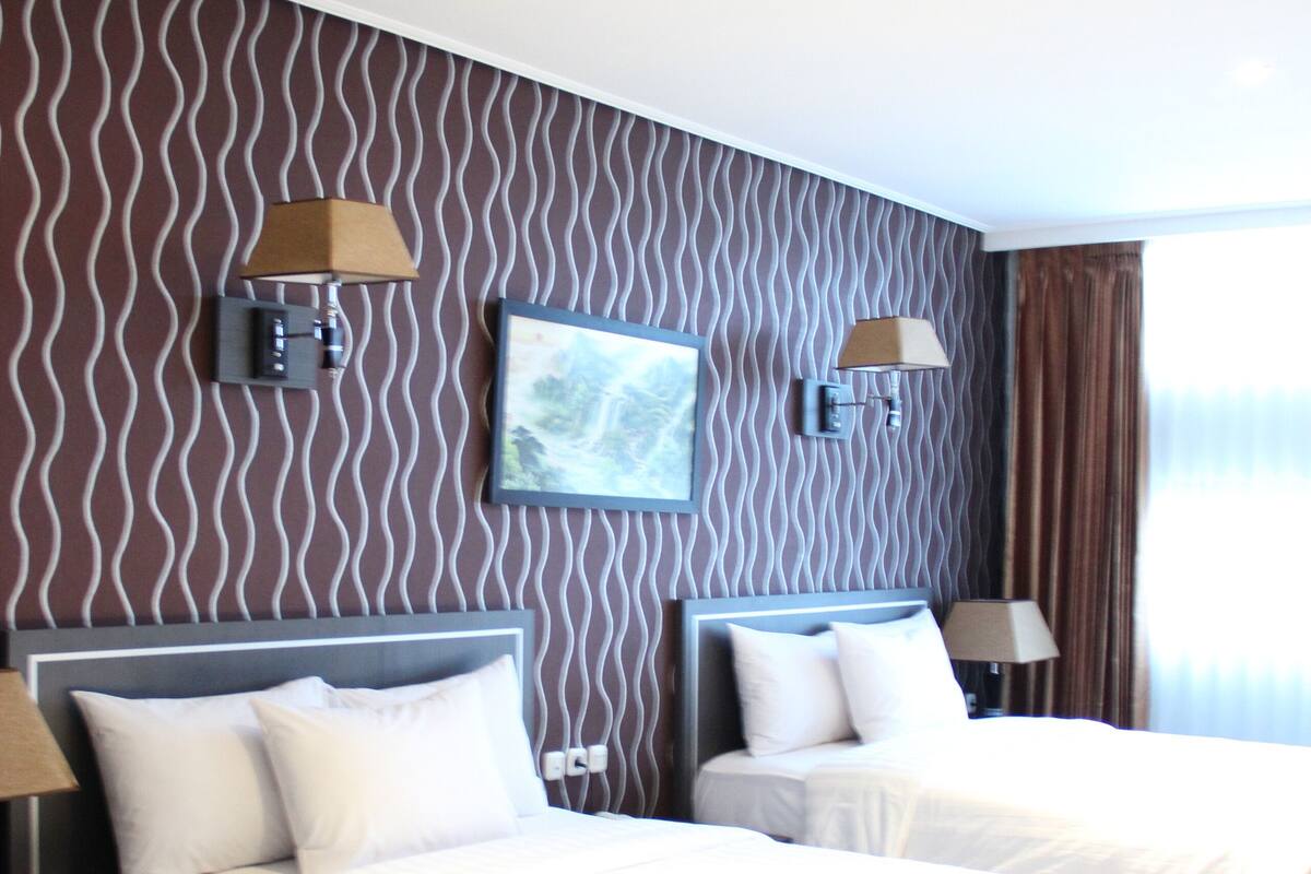 A hotel room with two beds, a large window, and a wavy-patterned wall.