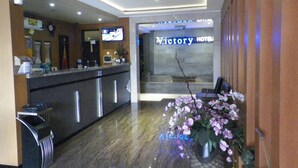 A hotel reception area with a reception desk, a television, and a sign for 'Victory Hotel'. - Hotel Victory Bandung (Bandung)