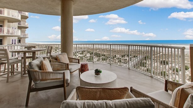 A spacious balcony with a view of the beach, furnished with wicker chairs and a round table.