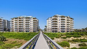 A wooden boardwalk leading to beachfront buildings with balconies and a clear sky.
