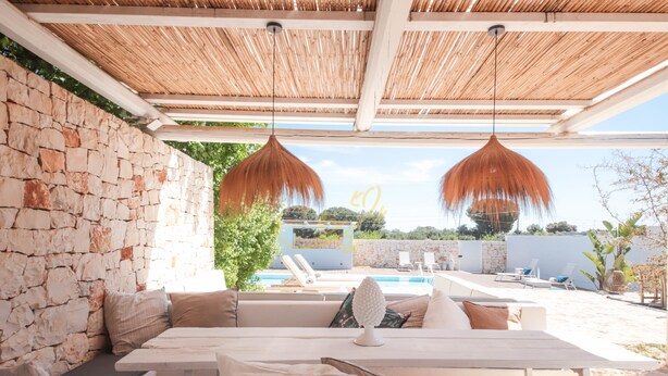 A covered outdoor seating area with stone walls, a pool, and hanging pendant lights. - TD Villa Fico Jo Villa with Pool & Lush Garden (Conversano)