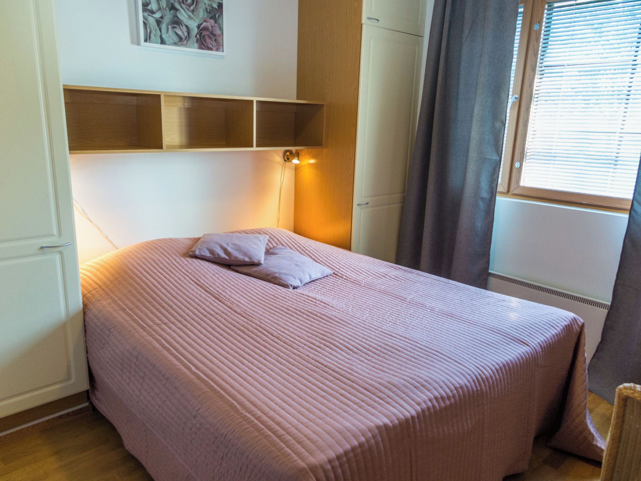 Una cama individual con cabecera, una lámpara de noche y una ventana con cortinas.