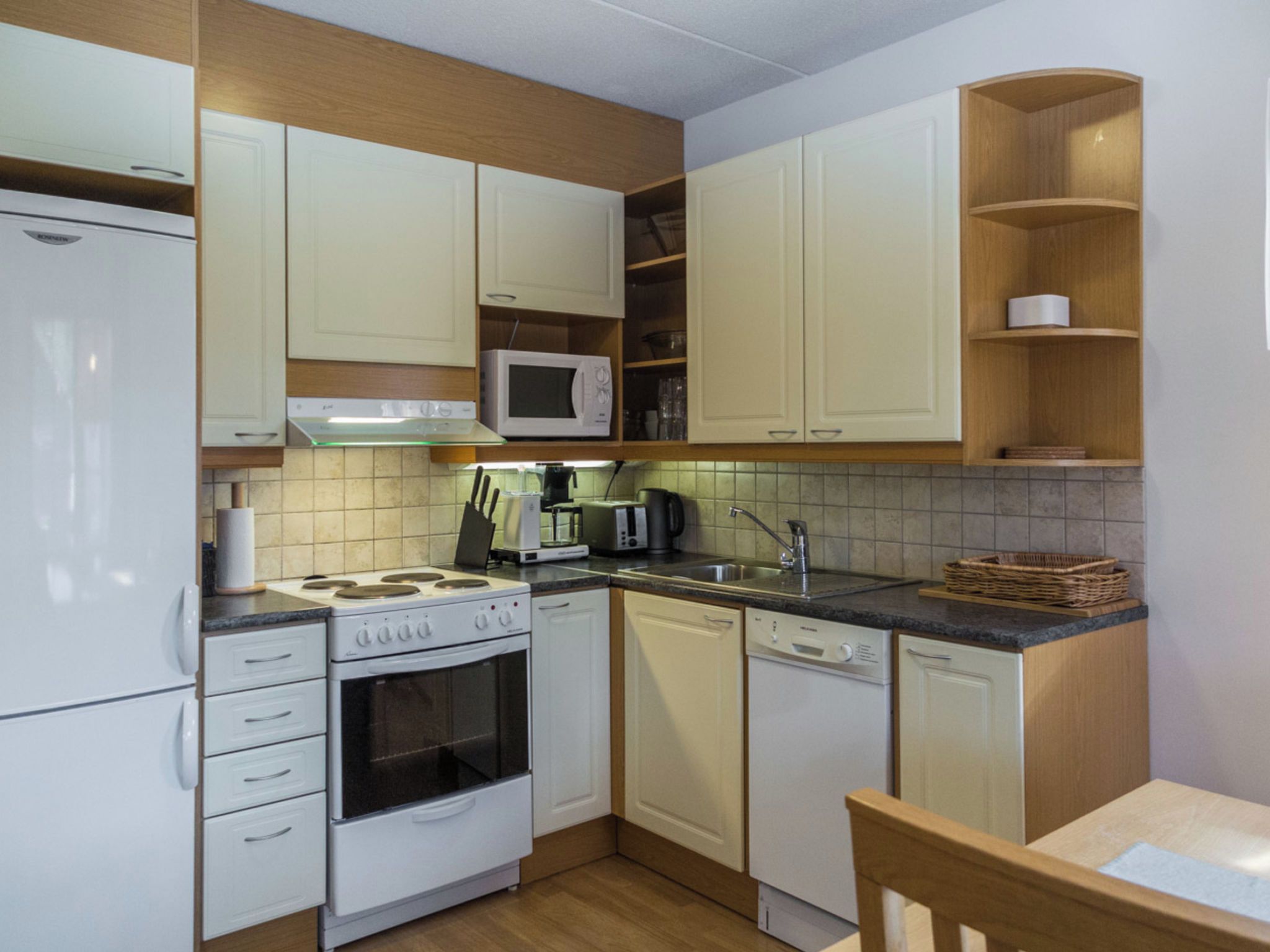 A compact kitchen with white appliances, wooden cabinetry, and a tiled backsplash.