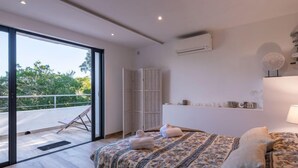 A modern bedroom with a large bed, a sliding glass door leading to a balcony, and an air conditioning unit on the wall.