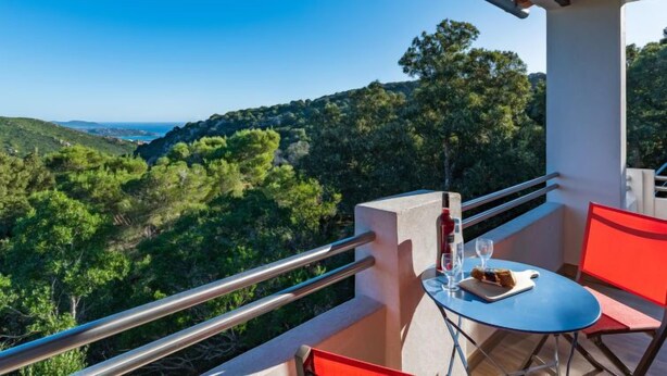 A balcony with a table and chairs, overlooking a mountainous landscape.