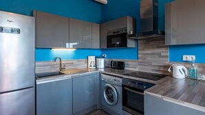 A modern kitchen with grey cabinets, a stainless steel refrigerator, a built-in oven, a microwave, and a washing machine.