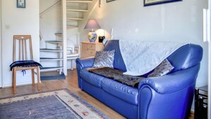 Un salon avec un canapé bleu, une chaise en bois, un escalier et un tableau accroché au mur.