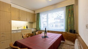 Cocina compacta con armarios de madera, una mesa de comedor con mantel rojo y una ventana con cortinas.