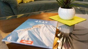 Una mesa de centro de vidrio con un libro titulado '4545' y una planta en maceta de hojas verdes y una flor rosa.