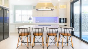 A modern kitchen with a central island, four black wire chairs, and a large window. - Pool Villa Pattaya - Exquisite Pool Villa H (Pattaya City)