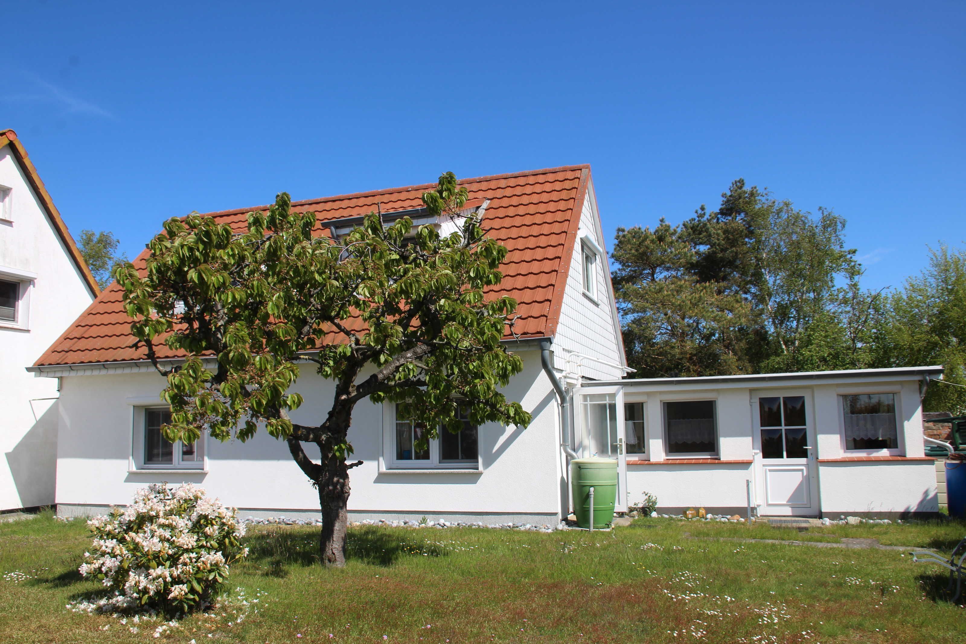 A white house with a red roof, a tree in front, and a green barrel.
