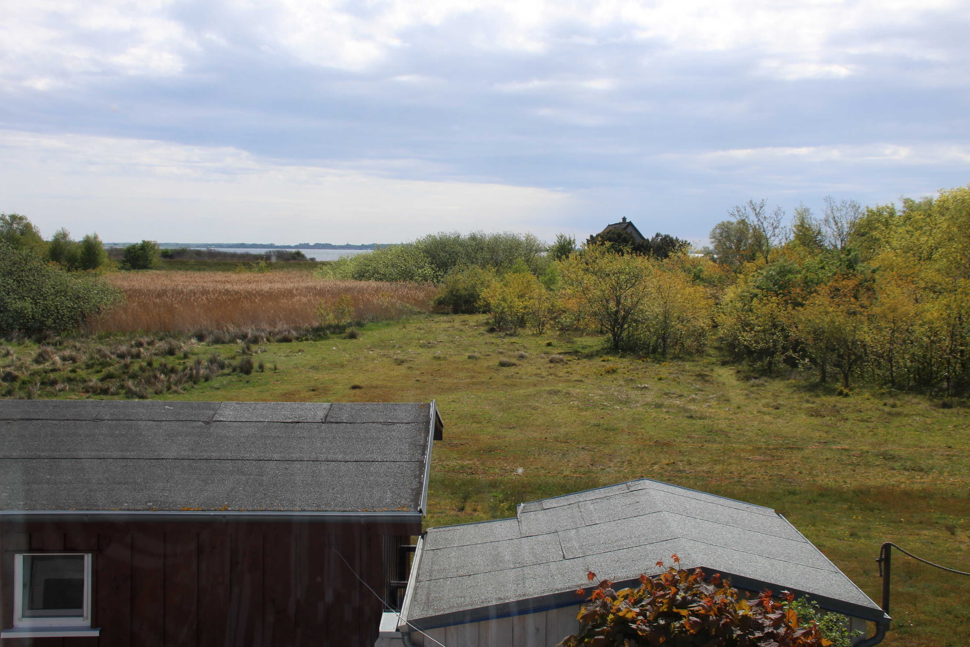 A view of a grassy field with a house in the foreground and a body of water in the distance.