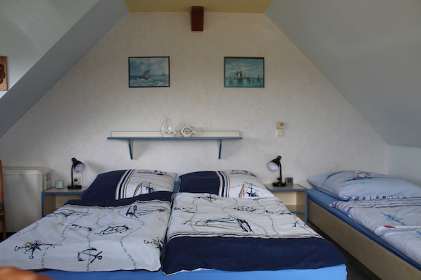Une chambre avec deux lits, un plafond en pente et deux tableaux encadrés accrochés au mur.