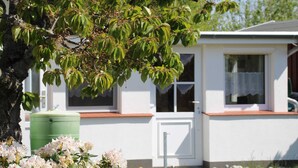 Uma casa móvel branca com janela e porta, um reservatório de água verde e uma árvore com folhas verdes.