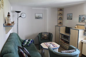 Una sala de estar acogedora con un sofá verde, una mesita, una silla, una estantería y un reloj en la pared.