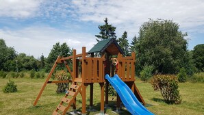 A wooden playground structure with a slide and climbing area, surrounded by grass and trees. - Ferienwohnung Mohnblume (Gerswalde)