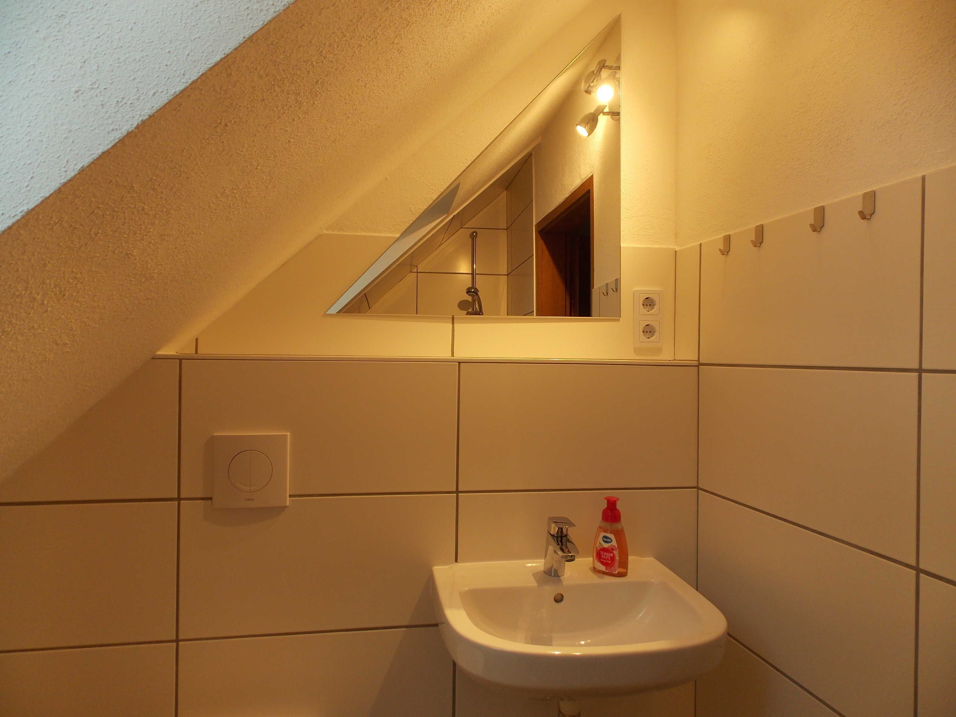 Un baño con lavamanos blanco, espejo y toallero.
