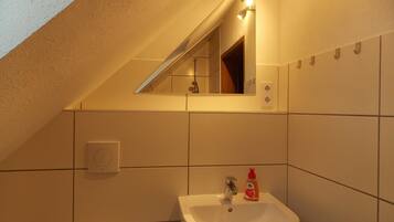 Un baño con lavamanos blanco, espejo y toallero.