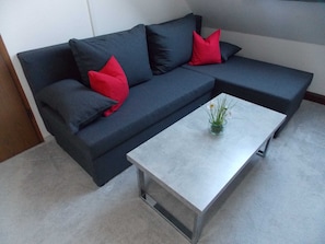 A dark-colored sofa with red cushions, a small glass vase with green plants, and a white coffee table. - Ferienwohnung Mohnblume (Gerswalde)