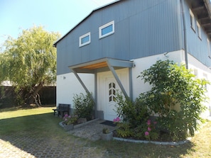 A two-story building with a grey exterior and white lower section. There is a covered porch with a bench and potted plants. - Ferienwohnung Mohnblume (Gerswalde)
