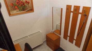 Et lille badeværelse med en radiator, et træskab, et spejl og en bruseholder.