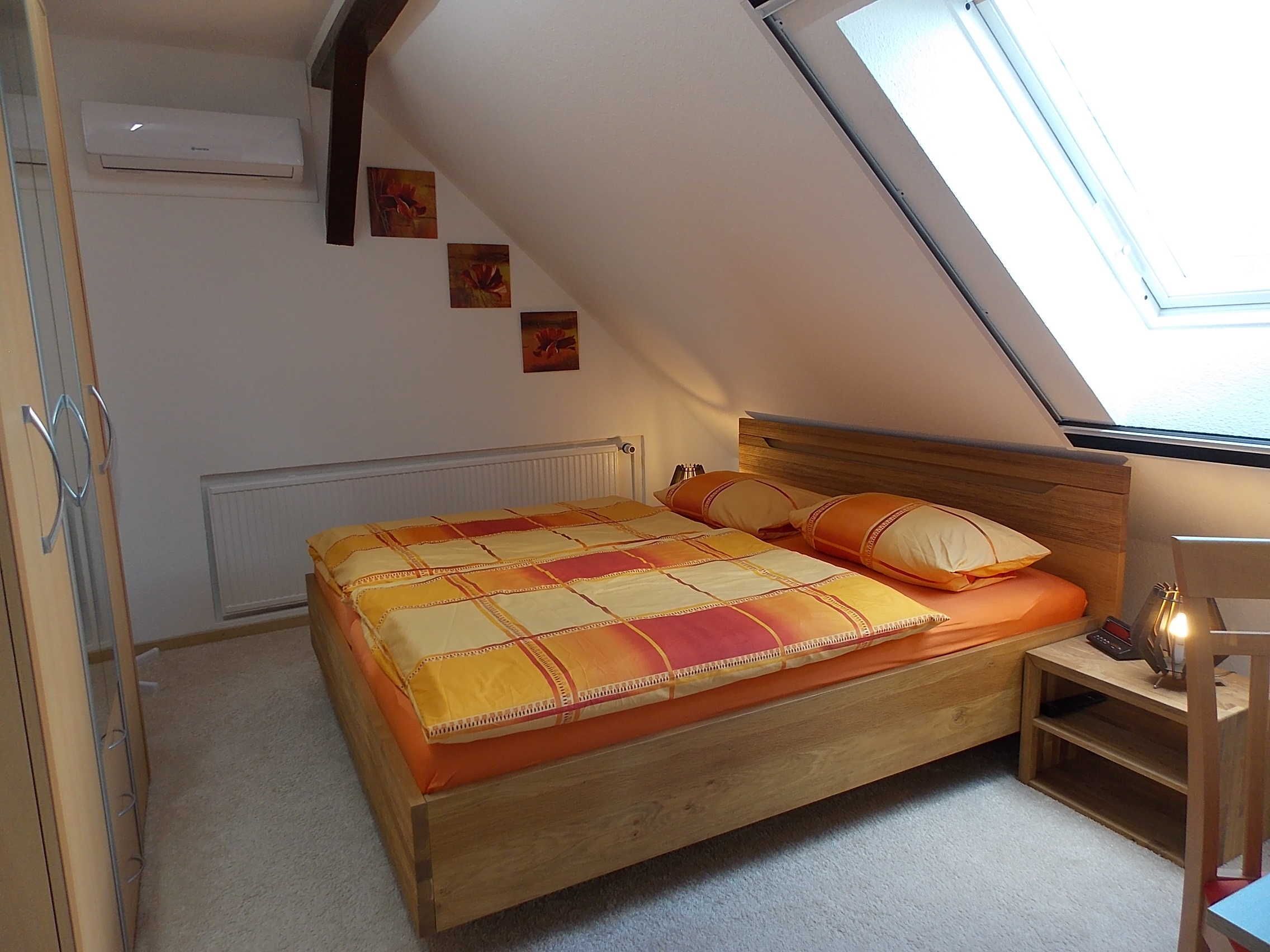 Un dormitorio con techo inclinado, una cama con colcha, una mesita de noche con lámpara y un radiador.
