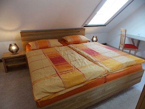 A bedroom with a large bed, two bedside tables, a nightstand, a wooden headboard, a skylight, and a chair. - Ferienwohnung Mohnblume (Gerswalde)