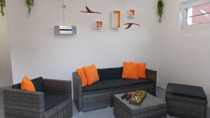 A modern lounge with wicker furniture, a central sofa with orange cushions, and decorative wall art. - Ferienwohnung Mohnblume (Gerswalde)