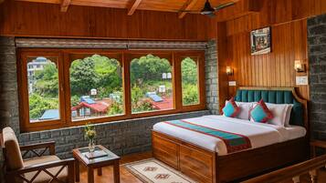 A bedroom with a large bed, wooden walls, a stone fireplace, and a view of green trees and buildings.