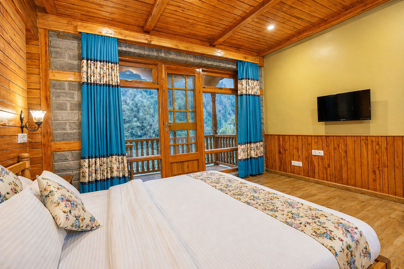 A wooden-paneled room with a bed, a television, and a balcony with blue curtains.