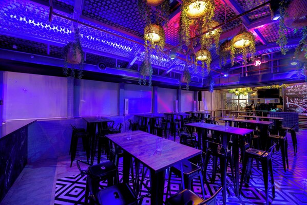 A restaurant with multiple tables and chairs, hanging decorations, and a patterned floor.