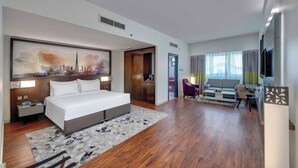 Et moderne hotelværelse med en stor seng, et skrivebord, en sofa og et bybillede på væggen.