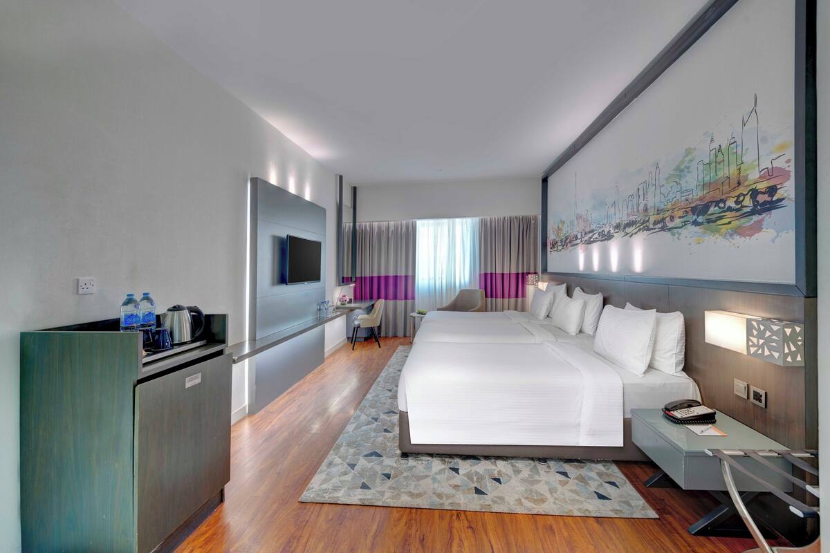 A modern hotel room with a large bed, a desk, a flat-screen TV, and a minibar.
