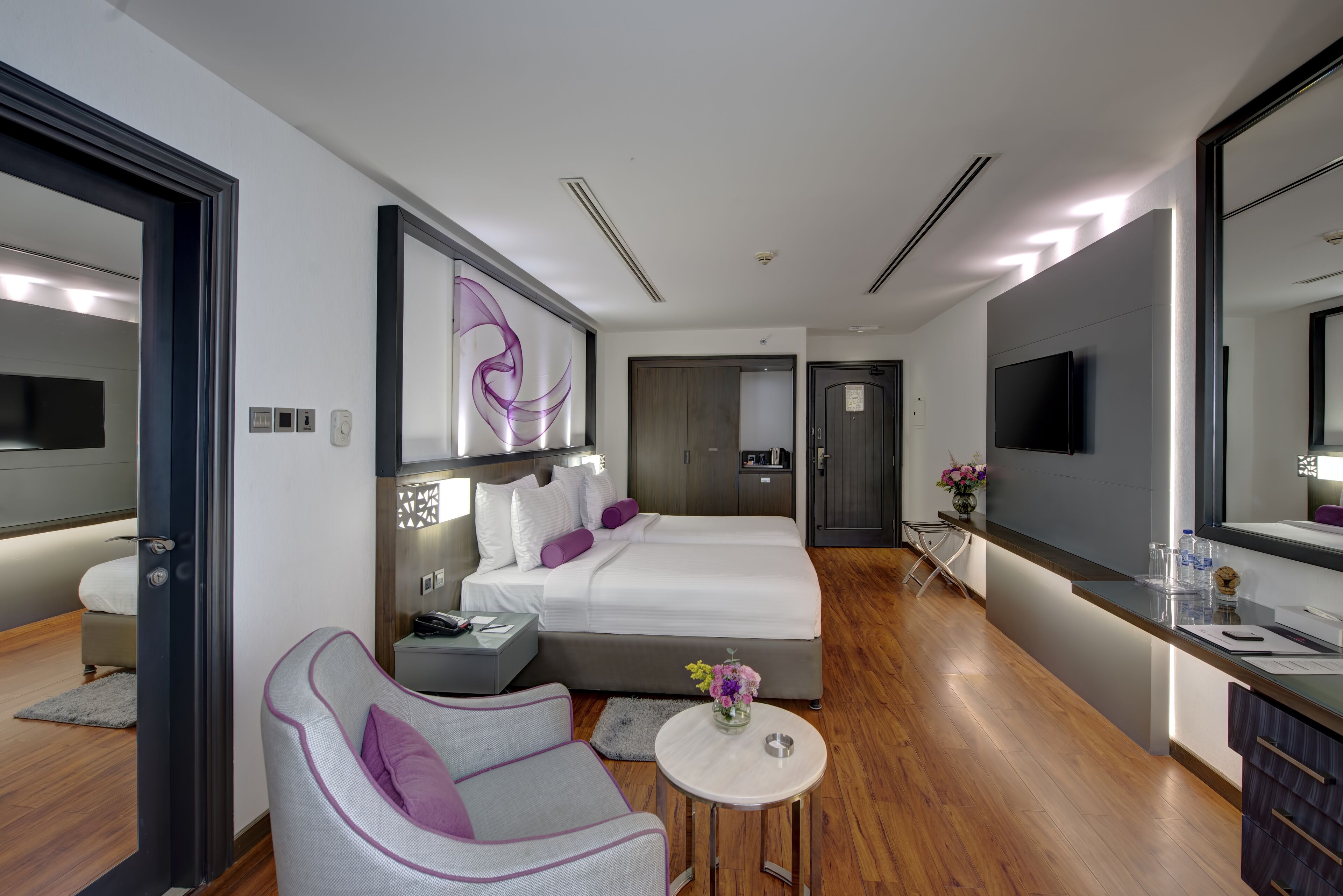 A modern hotel room with a large bed, a sofa, a small table with a vase, and a TV.