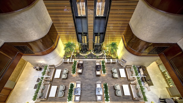En rummelig lobby med flere siddeområder, en central trappe og et dekorativt loft.