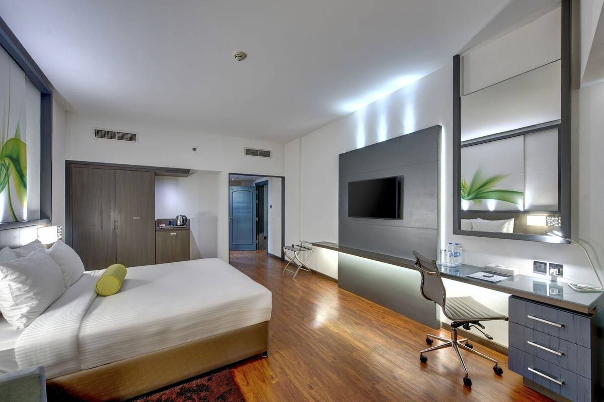 A modern hotel room with a bed, desk, chair, TV, and a large mirror.