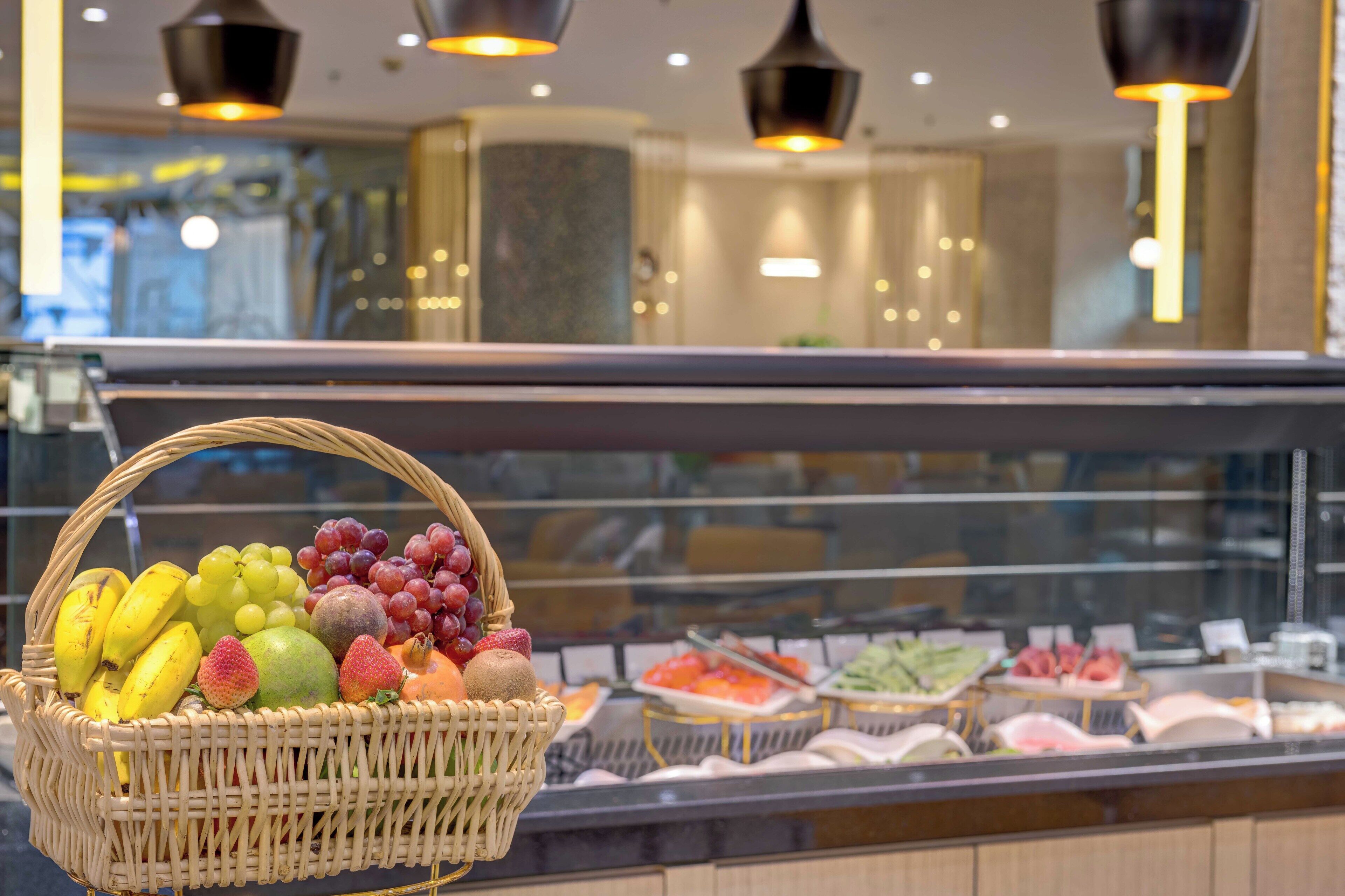 A buffet area with a wicker fruit basket containing bananas, grapes, apples, and kiwi.