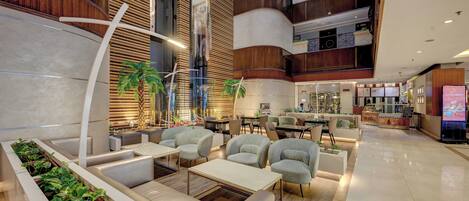 A modern hotel lobby with a central seating area, multiple floors, and a restaurant.