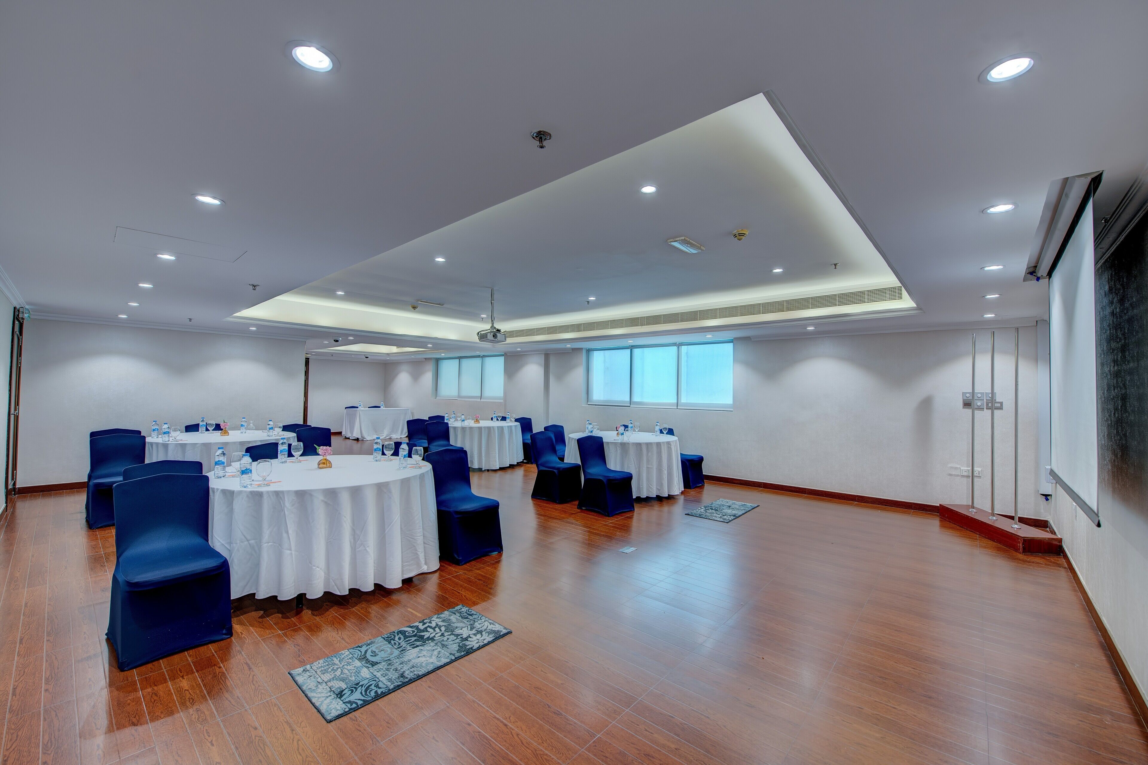 A conference room with round tables, blue chairs, white tablecloths, and ceiling lights.