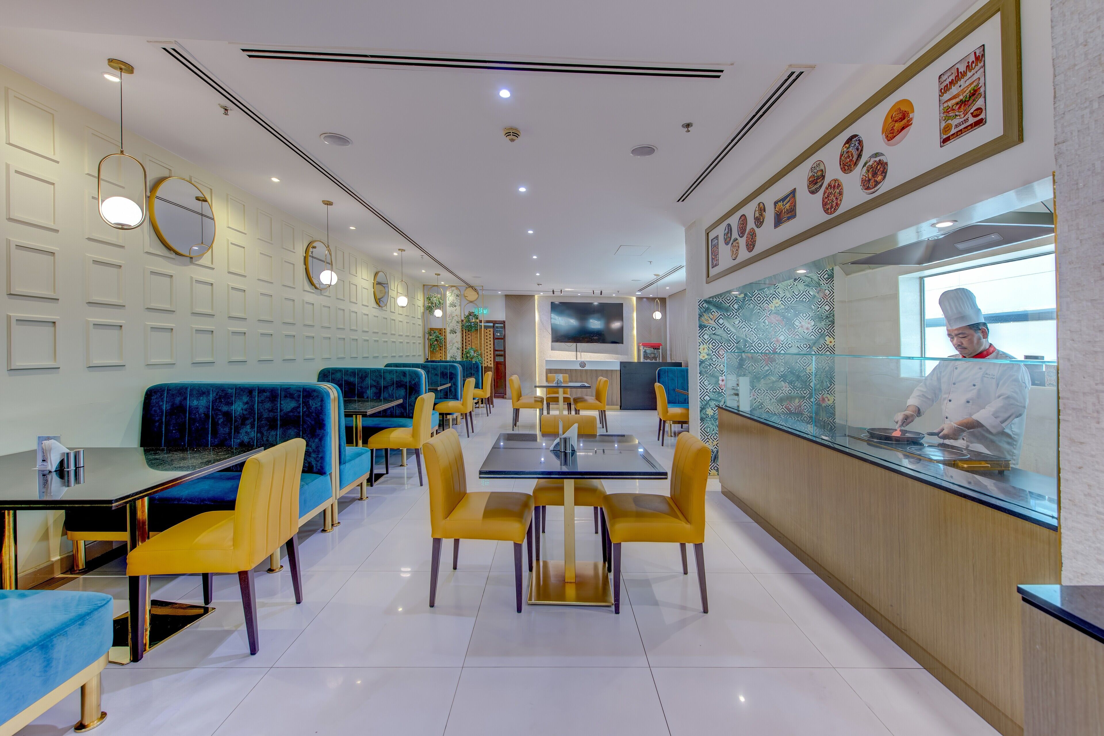 A modern restaurant with blue and yellow seating, a central dining area, and a counter with a chef.